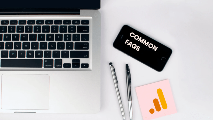 Workstation with a laptop, phone showing “Common FAQs,” pens, and a sticky note with the Google Analytics logo, representing frequently asked questions about setting up and using Google Analytics for Google Ads.
