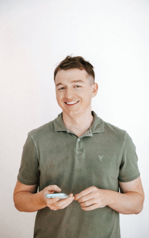 Ray Pastoors, A business professional wearing a green polo holding a smartphone while smiling at a camera against a white background.